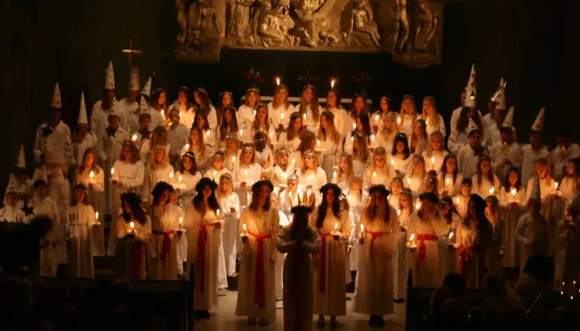 Stor kör av barn och ungdomar i vita dräkter med ljus och stjärnhattar under en luciakonsert 13 december i Stockholm.
