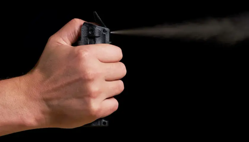 Main d'une personne actionnant une bombe lacrymogène, le jet de gaz se dispersant dans l'air. La loi encadre l'usage de ce type de défense.