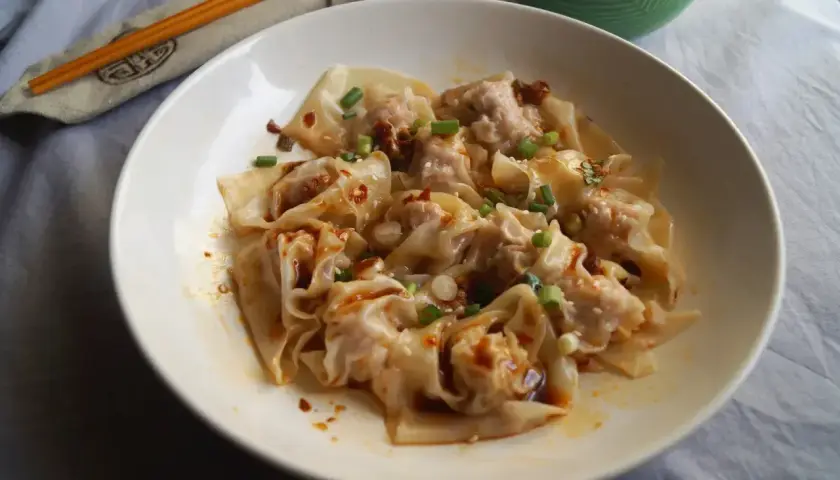 Pyszne ciasto wonton w pikantnym sosie, posypane szczypiorkiem i sezamem. Obok pałeczki w etui.