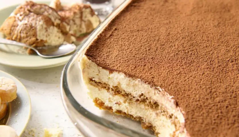 Najprostsze tiramisu w szklanej formie, posypane kakao. Na talerzyku porcja deseru i łyżeczka.