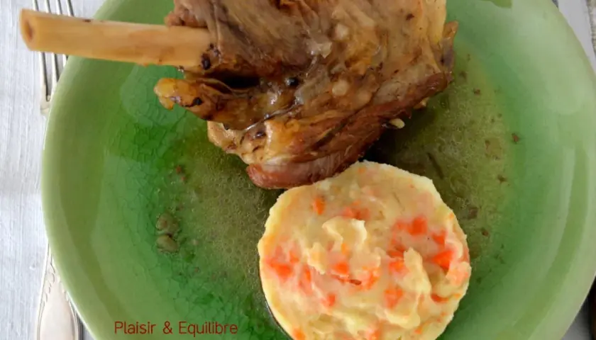 Souris d'agneau confite, tendre et savoureuse, servie avec une purée de carottes onctueuse sur une assiette verte craquelée.