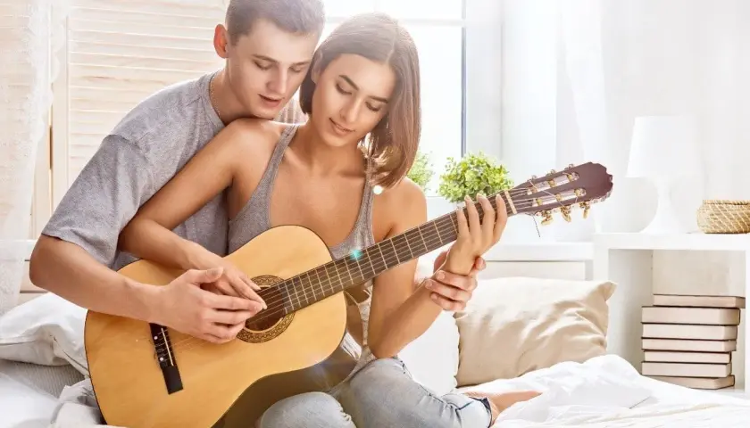 Para tworzy najpiękniejsze melodie o miłości, grając razem na gitarze w przytulnym pokoju.
