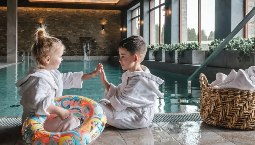 Dzieci w szlafrokach przy basenie, gotowe na wakacje w górach z dziećmi. Zabawa i relaks w górskim spa.
