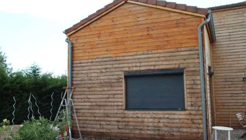 Échelle près d'un mur en bois, suggérant un entretien du bardage bois. Le bois est plus clair en haut, plus foncé en bas.