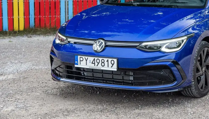 Niebieski Volkswagen z rejestracją PY 49819 stoi przed kolorowym płotem.