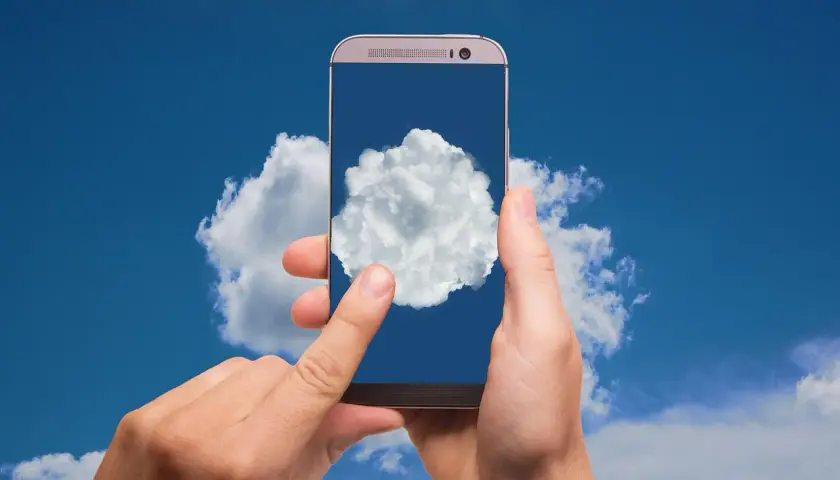 Dłonie trzymają telefon, na którego ekranie widać chmurę. To symbol tego, gdzie jest chmura w telefonie – w chmurze danych.