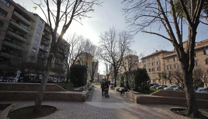 Passeggiata in un parco urbano, ideale per capire come arrivare a Testaccio da Termini. Alberi spogli, palazzi e persone con un passeggino.