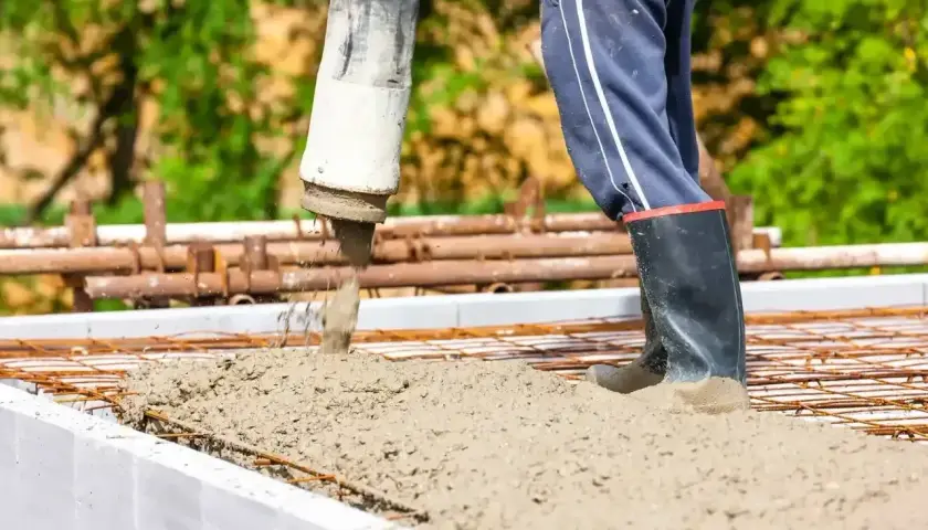 Beton wylewany jest na zbrojenie w szalunku. Pracownik w gumowcach stoi w świeżym betonie.