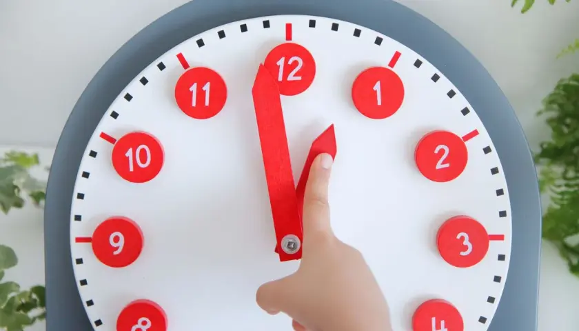 Un niño aprende las horas con un reloj didáctico. Las manecillas rojas apuntan a las 12 y las 11.