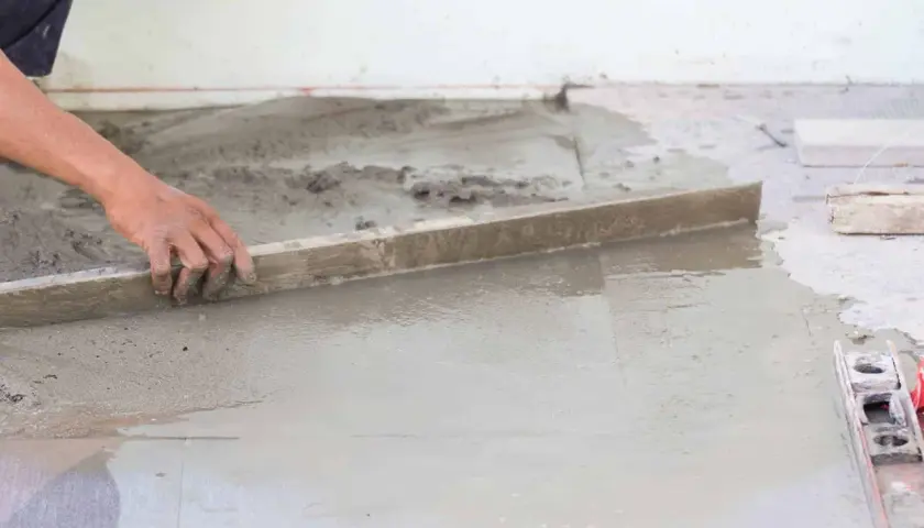 Ręka pracownika wyrównuje świeżą wylewkę betonową. Zastanawiasz się, ile waży wylewka betonowa?