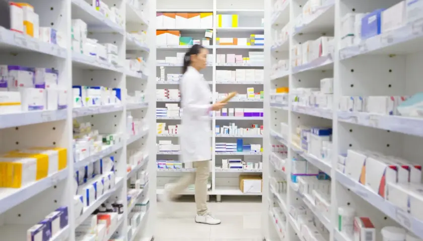 Farmaceutka w białym fartuchu przeszukuje półki apteki, szukając leku milurit 300.