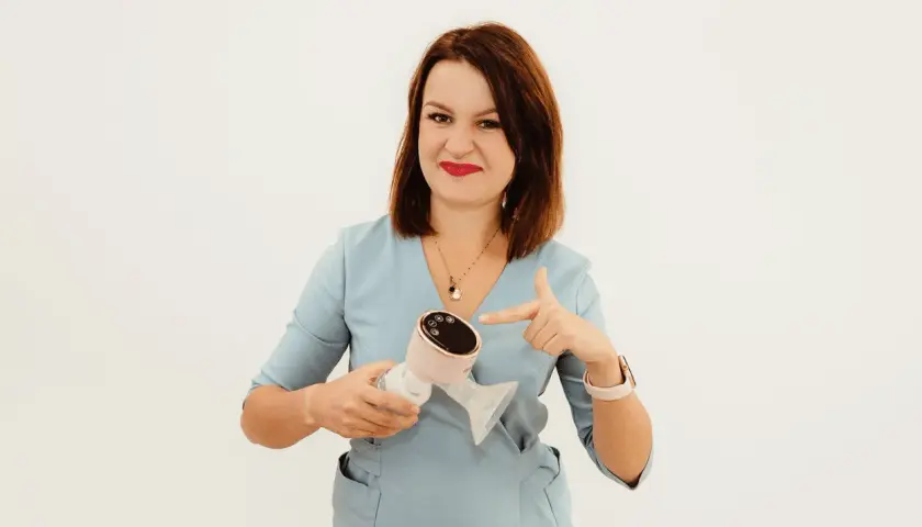 Kobieta w niebieskim uniformie wskazuje na nowoczesny laktator. To urządzenie, które może ułatwić życie mamom, jak i pomóc w pielęgnacji skóry, np. przy problemach z cerą, gdzie milanella complex jest często polecany.