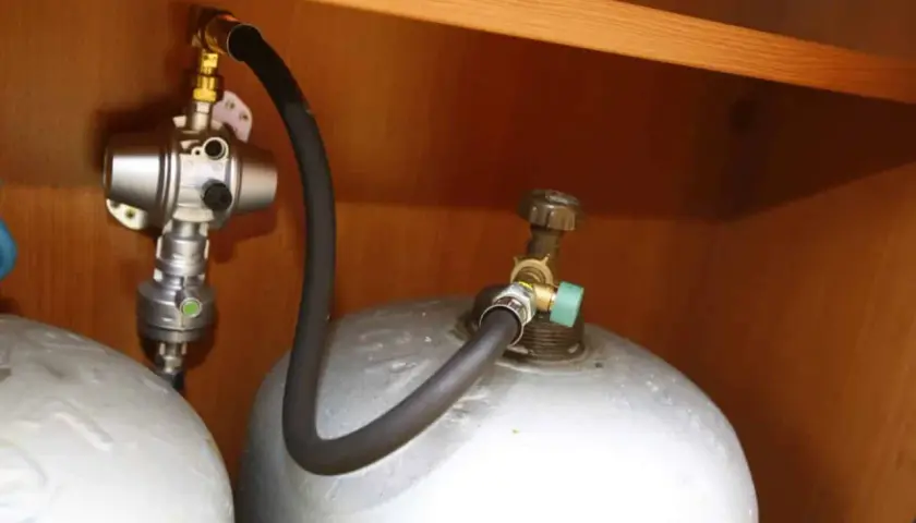 Connexion pour remplir bouteille de gaz au GPL. Tuyau noir relié à une valve verte sur la bouteille.