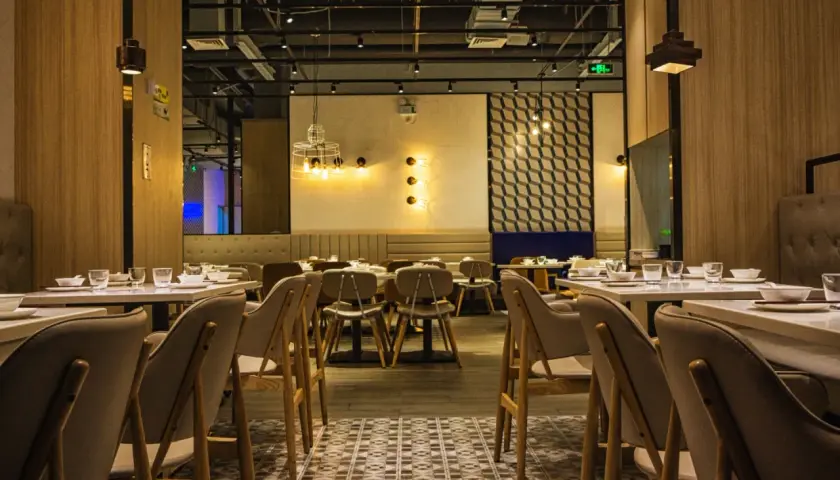 Przytulne wnętrze restauracji z drewnianymi panelami i stylowym oświetleniem. Stoliki nakryte, gotowe na gości.
