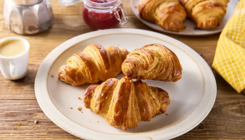 Talerz z trzema złotymi croissantami, filiżanka kawy, słoiczek dżemu i kawiarka.
