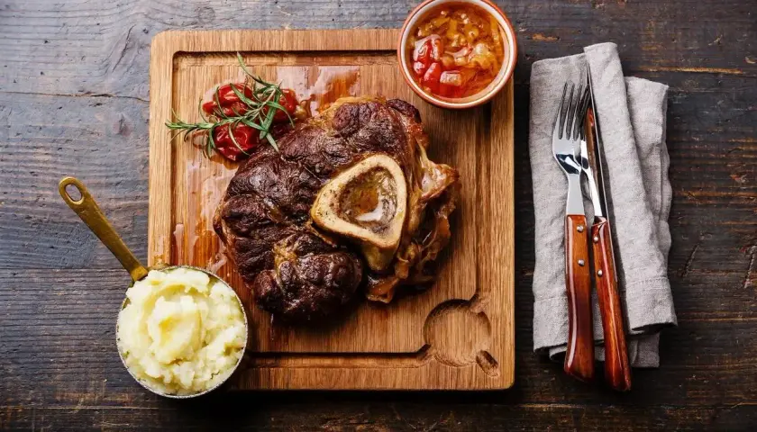 Wołowe ossobuco z puree ziemniaczanym, sosem i gałązką rozmarynu na desce.