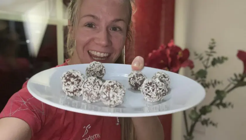 Glad kvinna visar en tallrik med nyttiga chokladbollar täckta av kokos. Perfekt för löpare!