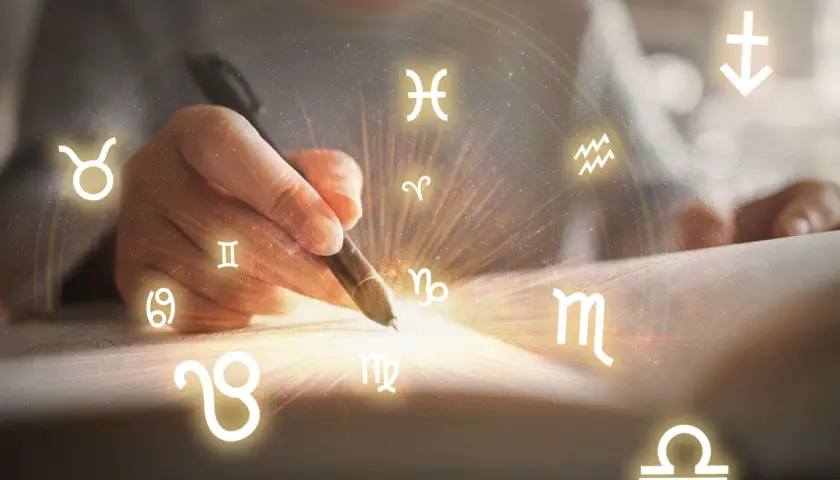 Dłoń pisze piórem, a wokół niej krążą wszystkie znaki zodiaku, tworząc magiczny krąg.