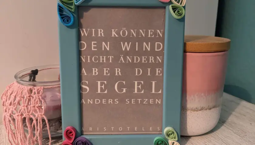 Ein hellblauer Bilderrahmen mit Quilling-Verzierungen, der ein Zitat von Aristoteles zeigt: "Wir können den Wind nicht ändern, aber die Segel anders setzen". Eine schöne alte Bilderrahmen Deko Idee.