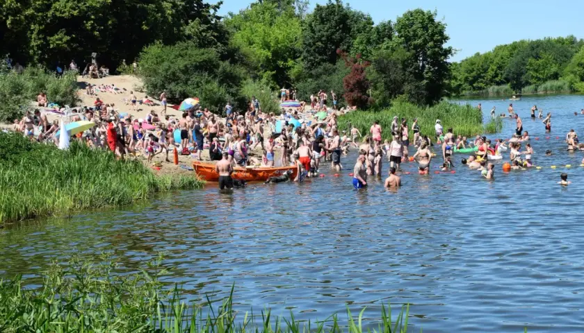 Tłum ludzi na plaży i w wodzie nad Jeziorkiem Czerniakowskim w słoneczny dzień.