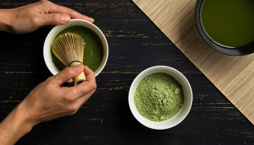 Hände bereiten Matcha zu. Pulver und fertiger Tee auf dunklem Holz. Eine positive matcha tee abnehmen erfahrung beginnt hier.