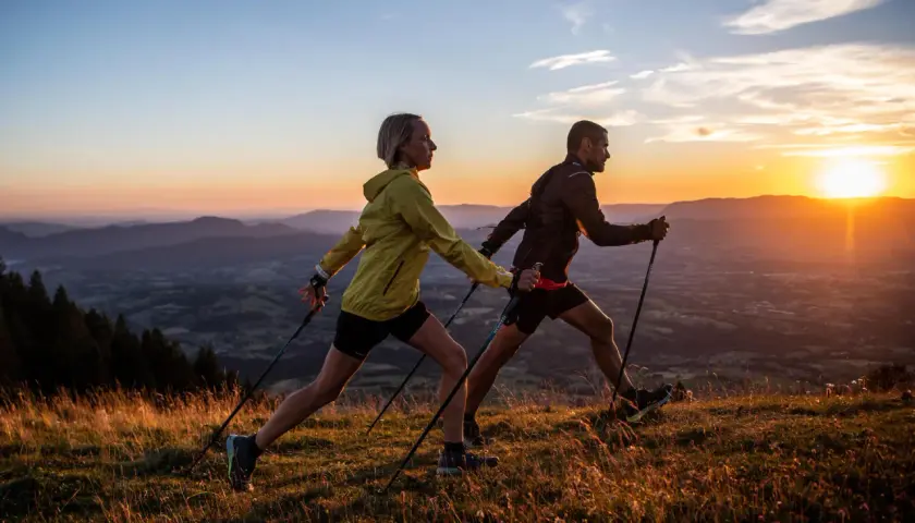 Para uprawiająca nordic walking na tle zachodzącego słońca nad górami.