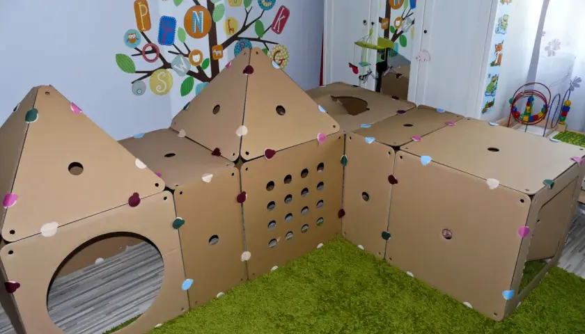 Kreatywne zabawki z kartonu diy tworzą domek do zabawy. Kolorowe serduszka zdobią kartonowe ściany, a otwory zapraszają do eksploracji.
