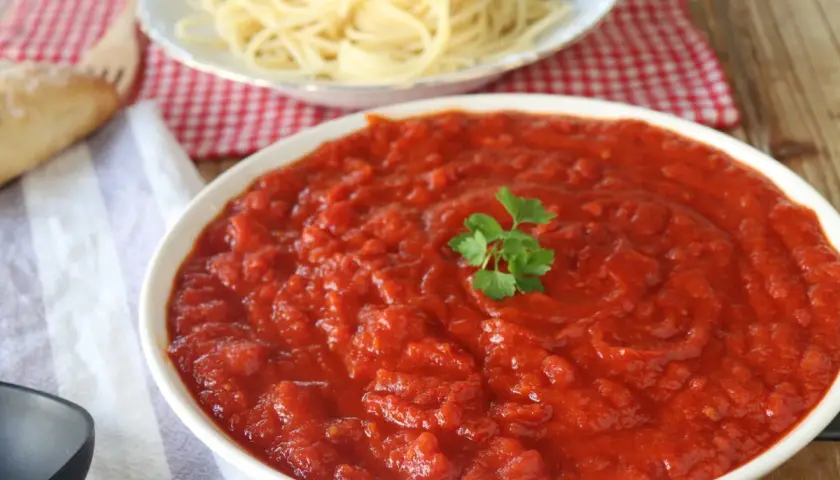 Un tazón de vibrante salsa arrabiata, decorado con perejil, junto a espaguetis y pan.