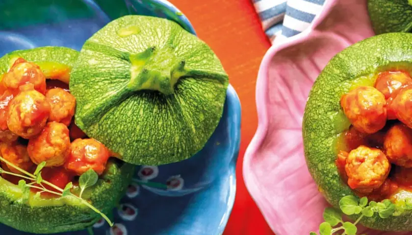 Zucchine tonde ripiene di polpettine in salsa, servite in ciotole colorate. Un piatto invitante e gustoso.