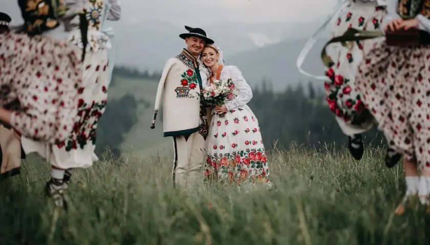 Para młoda w strojach góralskich z kapelą w tle, na tle górskiego krajobrazu.
