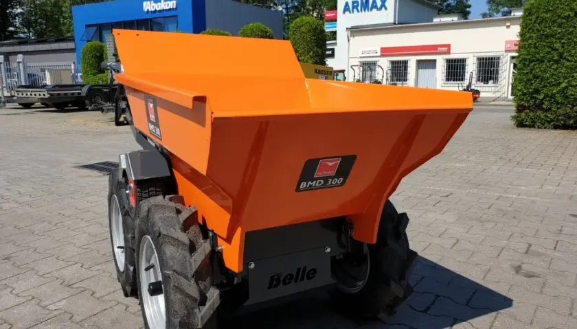 Pomarańczowe, małe wozidła budowlane stoją na placu przed budynkami.