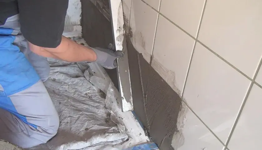 Hand mit Handschuh trägt Mörtel auf alte Fliesen auf, um eine Abdichtung zu schaffen.