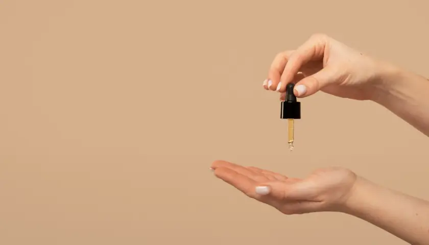 Una mano sostiene un gotero con aceite de jojoba para el pelo, listo para aplicarlo en la otra mano.