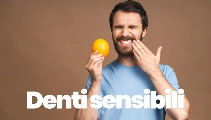 Uomo con espressione di dolore, tiene un'arancia e si tocca la guancia, soffre di sensibilità dentale.