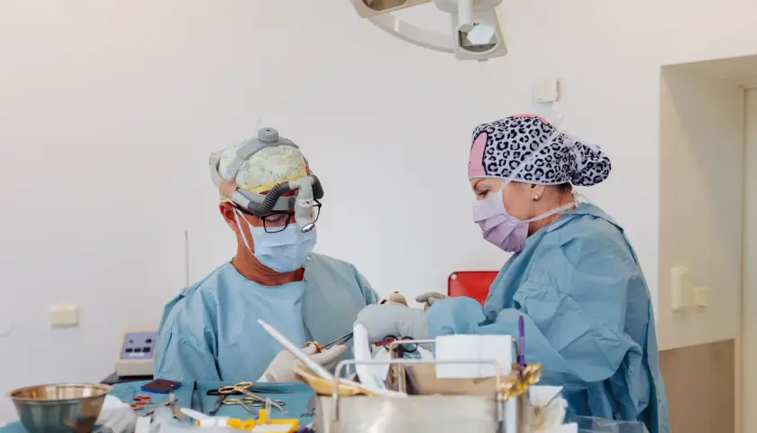 Två kirurger arbetar med instrument på ett bord. En av dem har en lampa på huvudet, vilket kan tyda på en komplicerad operation, kanske efter ett ansiktslyft.