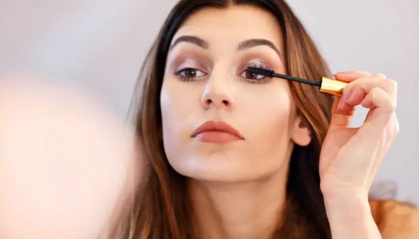 Une femme applique du mascara sur ses cils. Elle apprend comment mettre du mascara pour un regard intense.