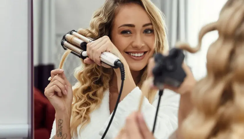 Uśmiechnięta blondynka tworzy sobie hollywoodzkie fale lokówką.