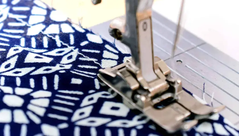 Sewing machine foot creating a narrow hem on a blue and white patterned fabric.