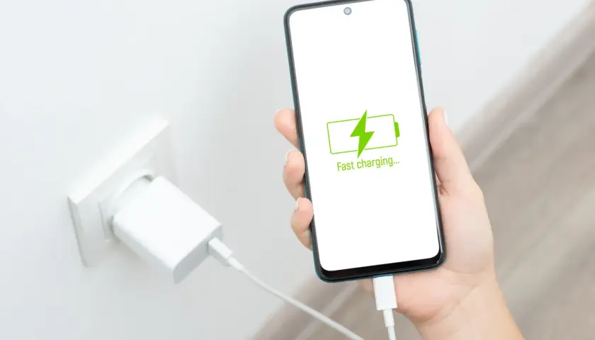 Dłoń trzyma smartfon z ikoną szybkiego ładowania. Czy szybkie ładowanie szkodzi baterii?
