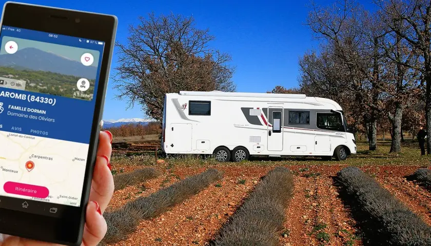 Une application camping-car à la ferme guide vers le Domaine des Oliviers. Un camping-car blanc est garé dans un champ de lavande séchée.