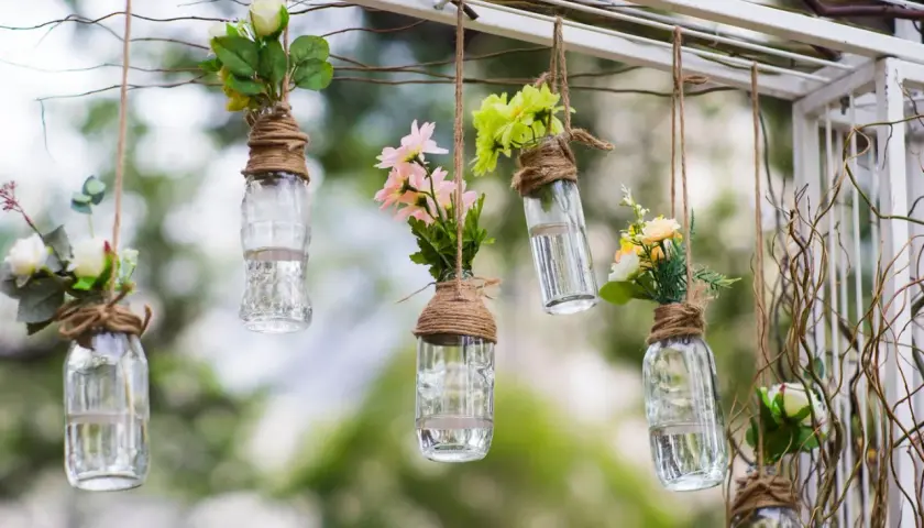 Upcycling ideen gartendeko selber machen: Hängende Glasflaschen mit Blumen als romantische Deko.