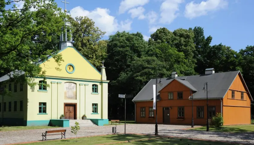 Żółty kościółek i pomarańczowy dom drewniany na tle zieleni i błękitnego nieba.