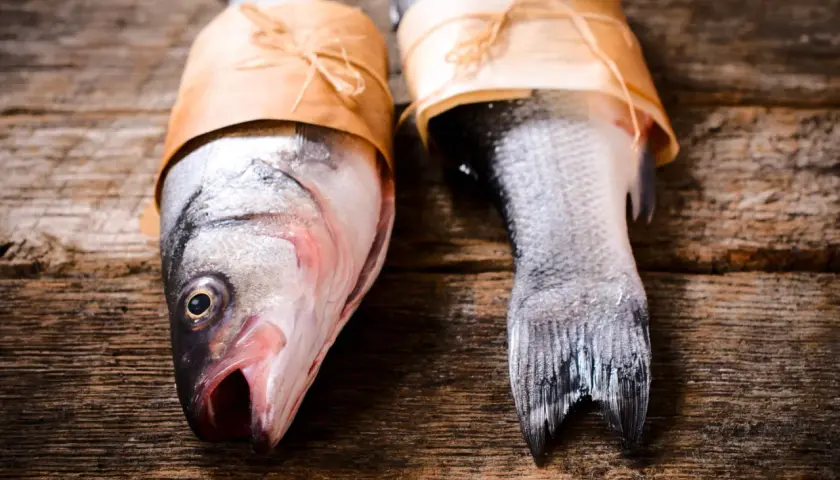 Deux poissons prêts pour le barbecue, emballés dans du papier kraft sur une table en bois rustique.