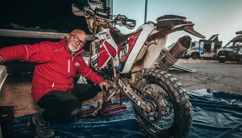 Uomo in giacca rossa vicino a moto da cross sporca, pronto a capire come pulire il motore dopo una gara.