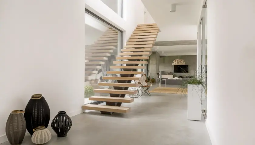 Nowoczesne schody z litego jesionu, unoszące się nad betonową posadzką, tworzą lekkość i elegancję.