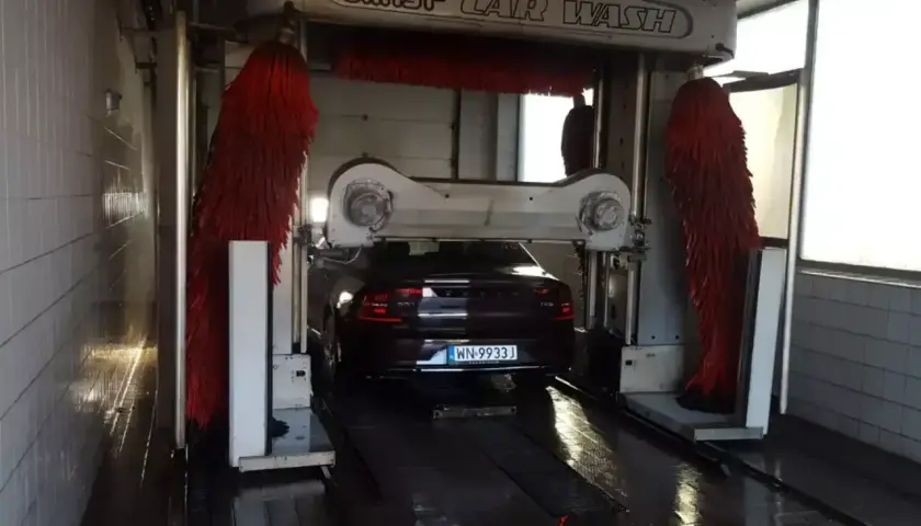 Ciemny Volvo czeka na mycie auta w automatycznej myjni. Czerwone szczotki są gotowe do pracy.