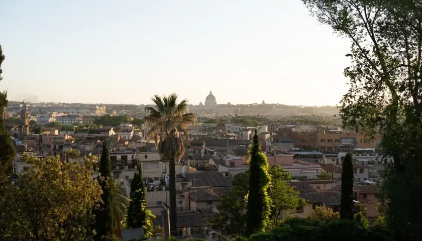 Panoramic view of Rome with St. Peter's Basilica dome in the distance, framed by trees and greenery.