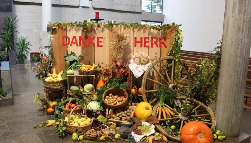 Erntedank: "Danke Herr" steht auf Holz. Reichlich Obst, Gemüse, Brot und Wagenräder schmücken den Tisch.