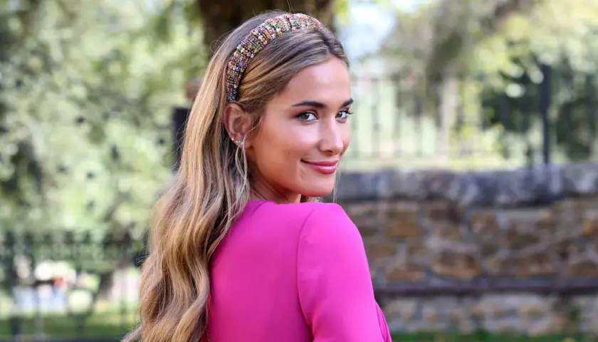 María Pombo, con un llamativo tocado de pedrería y un vestido fucsia, sonríe mirando por encima del hombro.