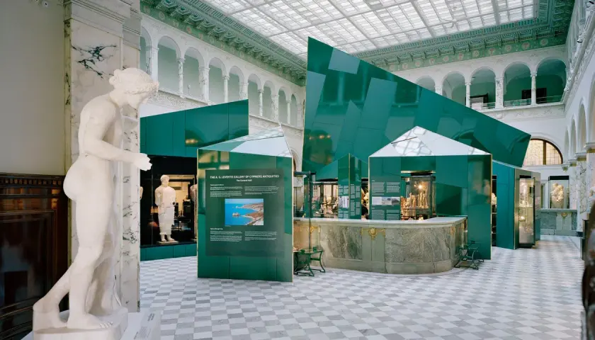 En marmorstaty i förgrunden på Medelhavsmuseet Stockholm. Gröna, geometriska installationer och antika föremål visas i den ljusa hallen.
